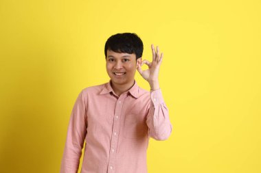 Sarı arka planda duran pembe gömlekli Asyalı adam..