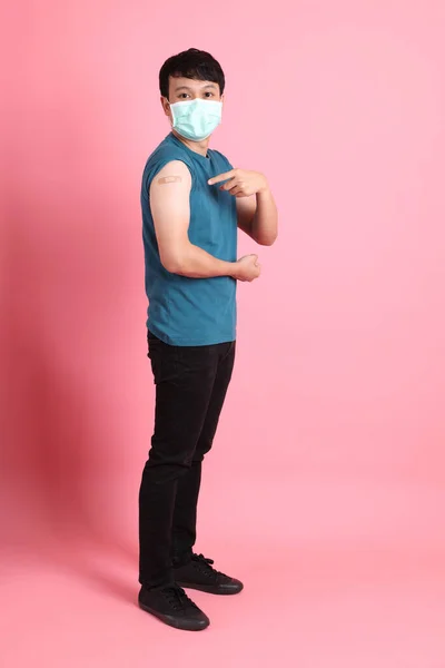 若いですアジアの男立っていますピンクの背景身に着けています保護マスクとともに包帯彼の腕に — ストック写真