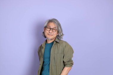 Mor arka planda dikilen sıradan giysili kıdemli Asyalı adam..