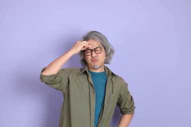 Mor arka planda dikilen sıradan giysili kıdemli Asyalı adam..