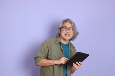 Mor arka planda dikilen sıradan giysili kıdemli Asyalı adam..