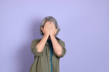 Mor arka planda dikilen sıradan giysili kıdemli Asyalı adam..