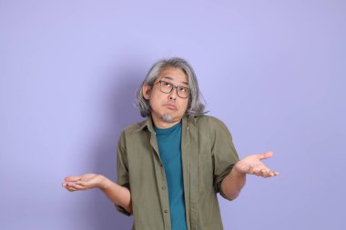 Mor arka planda dikilen sıradan giysili kıdemli Asyalı adam..