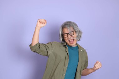 Mor arka planda dikilen sıradan giysili kıdemli Asyalı adam..