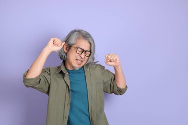 Mor arka planda dikilen sıradan giysili kıdemli Asyalı adam..