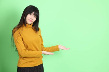 Yeşil arka planda sıradan giyinmiş, tatlı Asyalı genç kız.