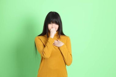 Yeşil arka planda sıradan giyinmiş, tatlı Asyalı genç kız.