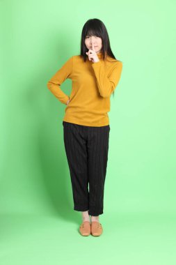 Yeşil arka planda sıradan giyinmiş, tatlı Asyalı genç kız.