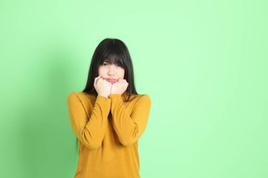 Yeşil arka planda sıradan giyinmiş, tatlı Asyalı genç kız.