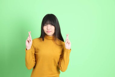 Yeşil arka planda sıradan giyinmiş, tatlı Asyalı genç kız.