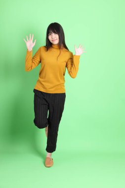 Yeşil arka planda sıradan giyinmiş, tatlı Asyalı genç kız.