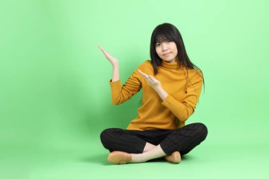 Yeşil arka planda oturan sıradan giyinmiş Asyalı genç kız..