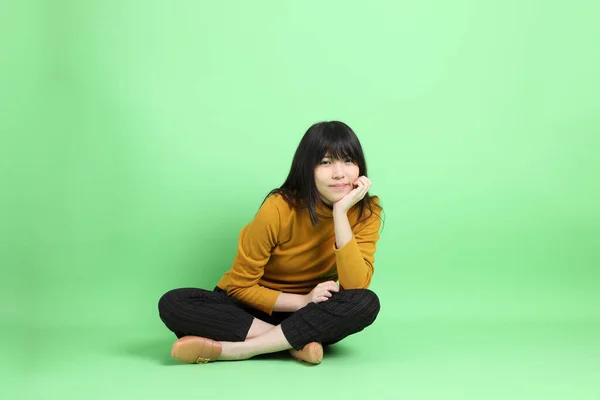 穿着休闲装的年轻亚洲女孩坐在绿色的背景上 — 图库照片