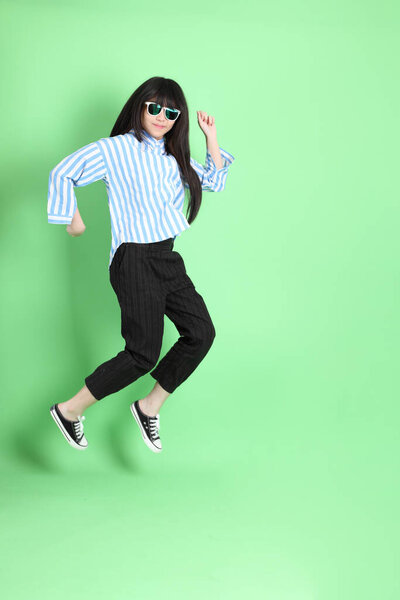 Молодая азиатка в солнечных очках, стоящая на зеленом фоне.