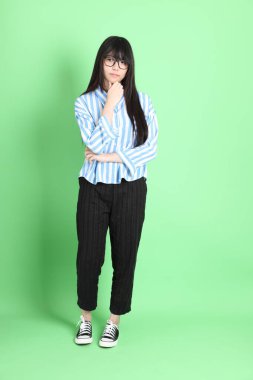 Yeşil arka planda sıradan giyinmiş genç Asyalı kız..