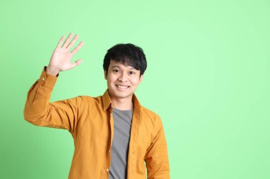 Açık yeşil arka planda duran şık günlük kıyafetleri olan genç Asyalı adam..