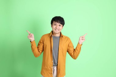 Açık yeşil arka planda duran şık günlük kıyafetleri olan genç Asyalı adam..