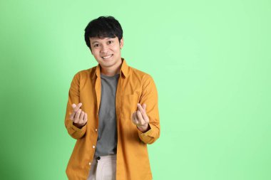 Açık yeşil arka planda duran şık günlük kıyafetleri olan genç Asyalı adam..