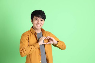 Açık yeşil arka planda duran şık günlük kıyafetleri olan genç Asyalı adam..