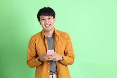 Açık yeşil arka planda duran şık günlük kıyafetleri olan genç Asyalı adam..