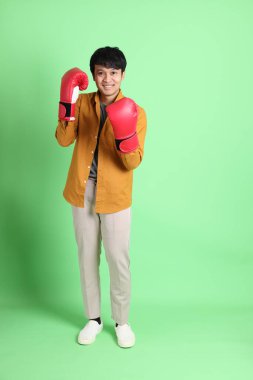 Açık yeşil arka planda duran şık günlük kıyafetleri olan genç Asyalı adam..