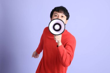 Açık yeşil arka planda duran kırmızı uzun kollu Güneydoğu Asyalı genç adam..