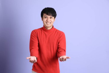 Açık yeşil arka planda duran kırmızı uzun kollu Güneydoğu Asyalı genç adam..