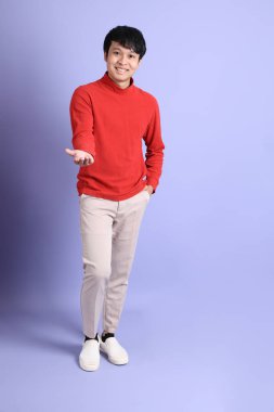 Açık yeşil arka planda duran kırmızı uzun kollu Güneydoğu Asyalı genç adam..