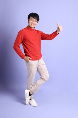 Açık yeşil arka planda duran kırmızı uzun kollu Güneydoğu Asyalı genç adam..