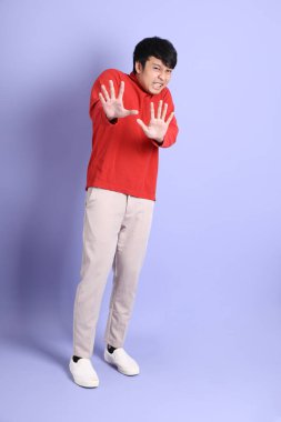 Açık yeşil arka planda duran kırmızı uzun kollu Güneydoğu Asyalı genç adam..