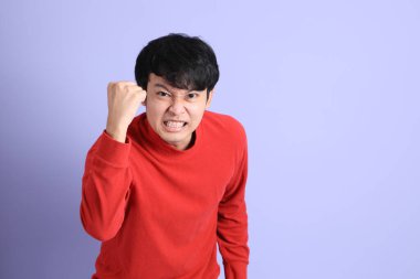 Açık yeşil arka planda duran kırmızı uzun kollu Güneydoğu Asyalı genç adam..