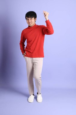 Açık yeşil arka planda duran kırmızı uzun kollu Güneydoğu Asyalı genç adam..