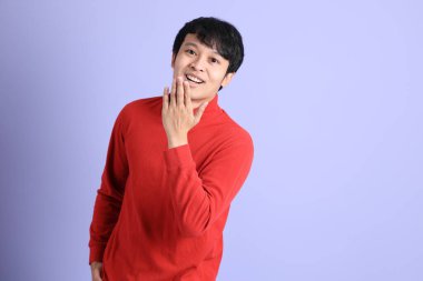 Açık yeşil arka planda duran kırmızı uzun kollu Güneydoğu Asyalı genç adam..