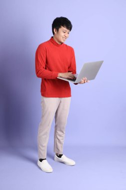 Açık yeşil arka planda duran kırmızı uzun kollu Güneydoğu Asyalı genç adam..