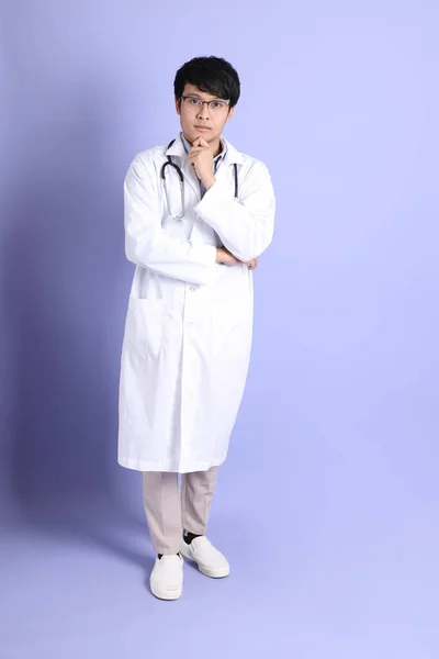 站在紫色背景上的年轻的亚洲医生 — 图库照片