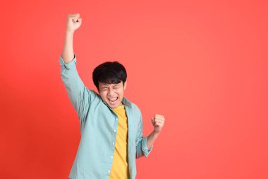 Turuncu arka planda duran yeşil tişörtlü Güneydoğu Asyalı genç adam..