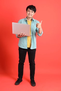 Turuncu arka planda duran yeşil tişörtlü Güneydoğu Asyalı genç adam..