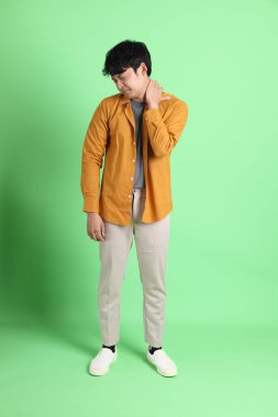 Açık yeşil arka planda duran şık günlük kıyafetleri olan genç Asyalı adam..