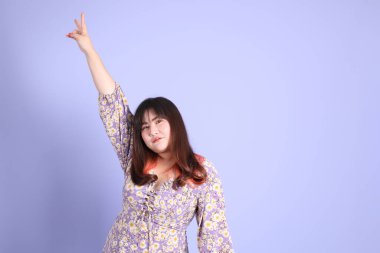 Mor arka planda sıradan kıyafetlerle duran tombul Asyalı kadın..