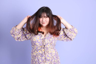 Mor arka planda sıradan kıyafetlerle duran tombul Asyalı kadın..