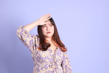 Mor arka planda sıradan kıyafetlerle duran tombul Asyalı kadın..