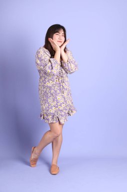 Mor arka planda sıradan kıyafetlerle duran tombul Asyalı kadın..