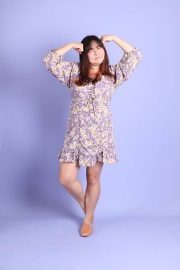 Mor arka planda sıradan kıyafetlerle duran tombul Asyalı kadın..