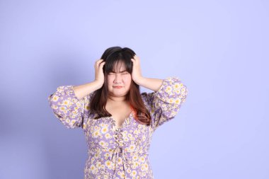 Mor arka planda sıradan kıyafetlerle duran tombul Asyalı kadın..