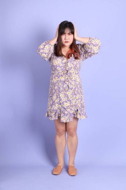 Mor arka planda sıradan kıyafetlerle duran tombul Asyalı kadın..