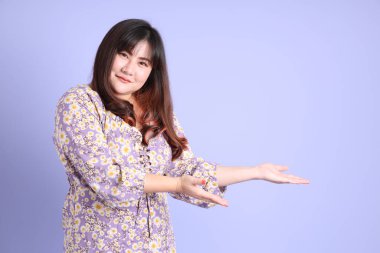 Mor arka planda sıradan kıyafetlerle duran tombul Asyalı kadın..