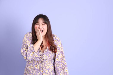 Mor arka planda sıradan kıyafetlerle duran tombul Asyalı kadın..