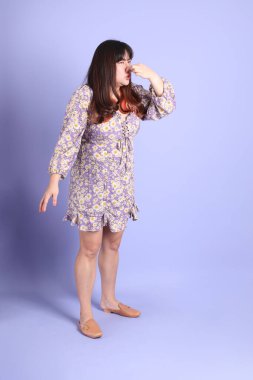 Mor arka planda sıradan kıyafetlerle duran tombul Asyalı kadın..