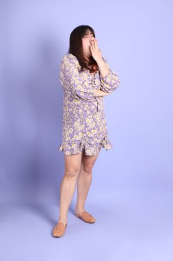 Mor arka planda sıradan kıyafetlerle duran tombul Asyalı kadın..