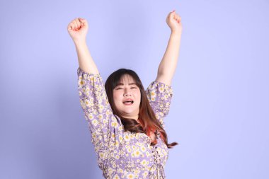 Mor arka planda sıradan kıyafetlerle duran tombul Asyalı kadın..